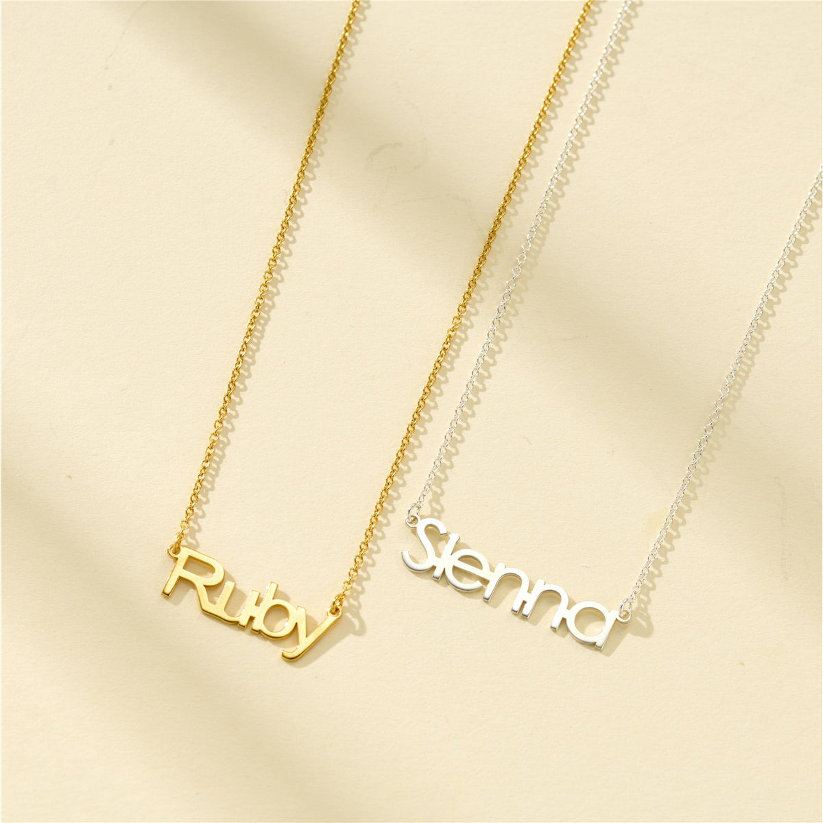 Yellow gold plated Ruby name necklace beside a silver Sienna name necklace
