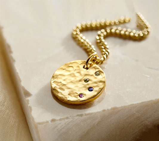 Gold textured Confetti Birthstone Disc Necklace with colourful gemstones on a pale stone surface.