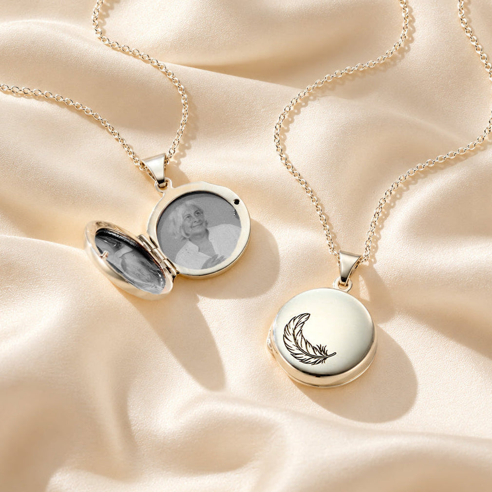 Personalised Feather Photo Locket Necklaces on cream satin, showing an open photo locket and engraved feather