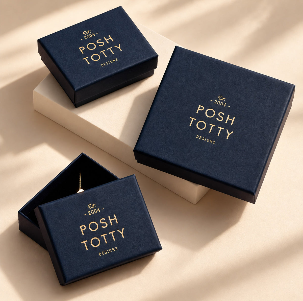 Navy Posh Totty Designs jewellery gift boxes with gold branding on a cream background.