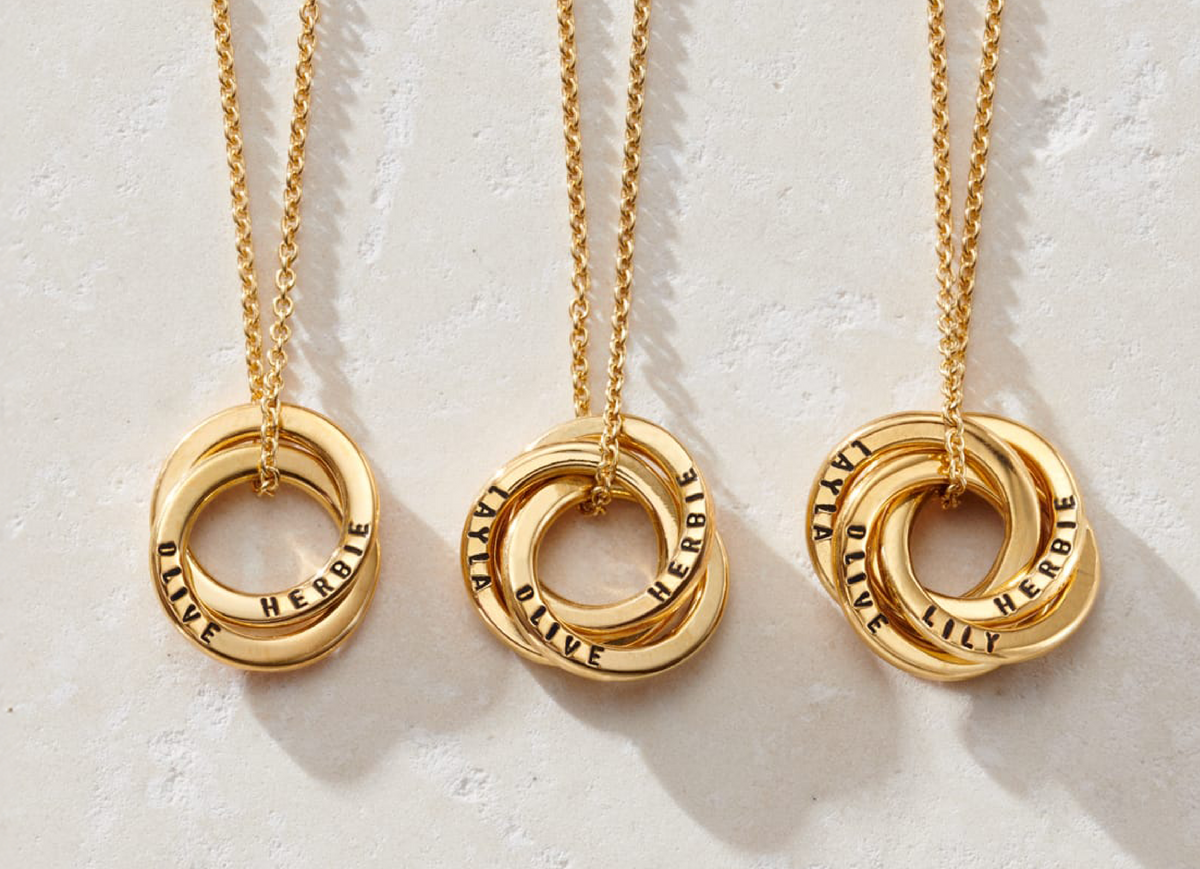 Three personalised gold Russian ring necklaces on pale fabric
